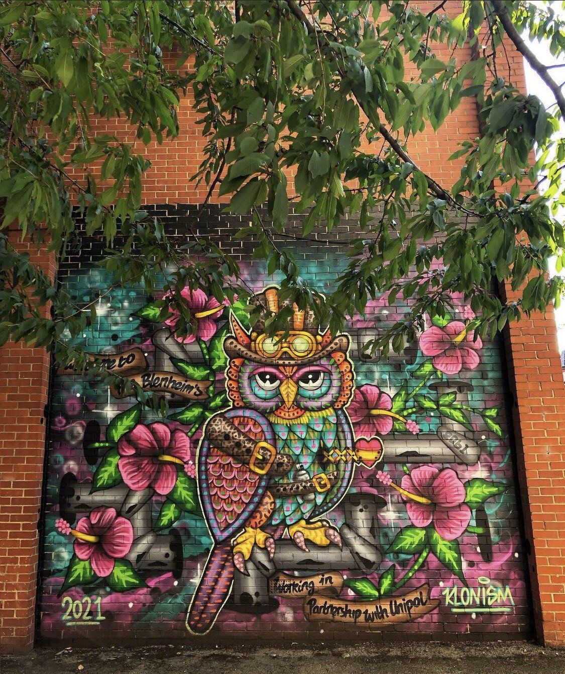 A mural of an owl wearing a crown on a brick wall.