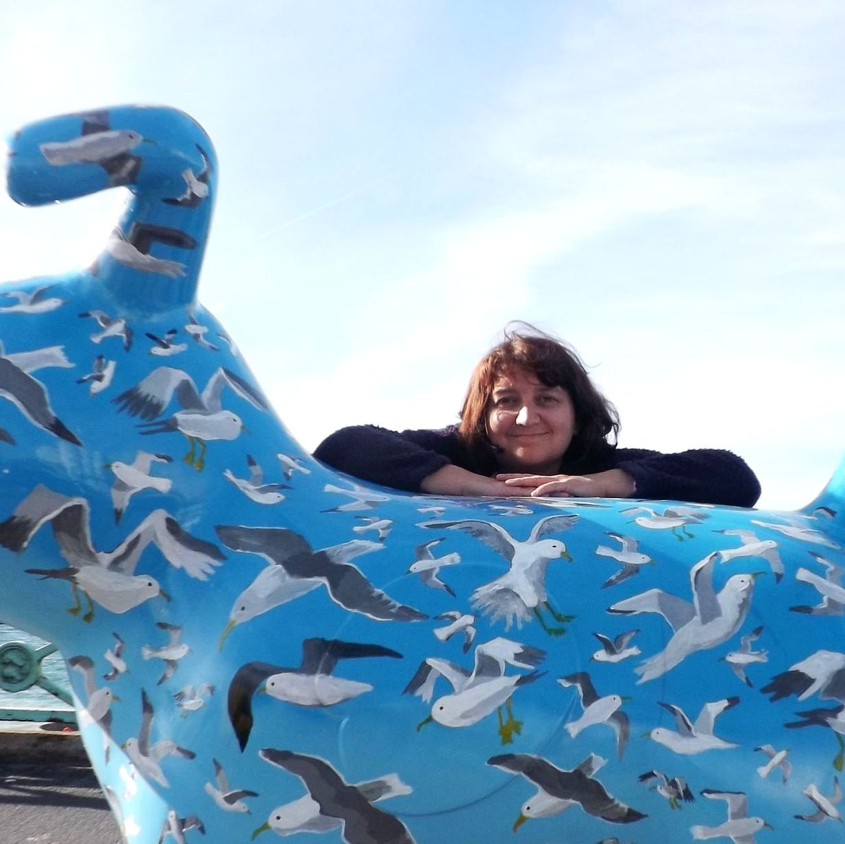 A woman is sitting on a blue statue with seagulls on it