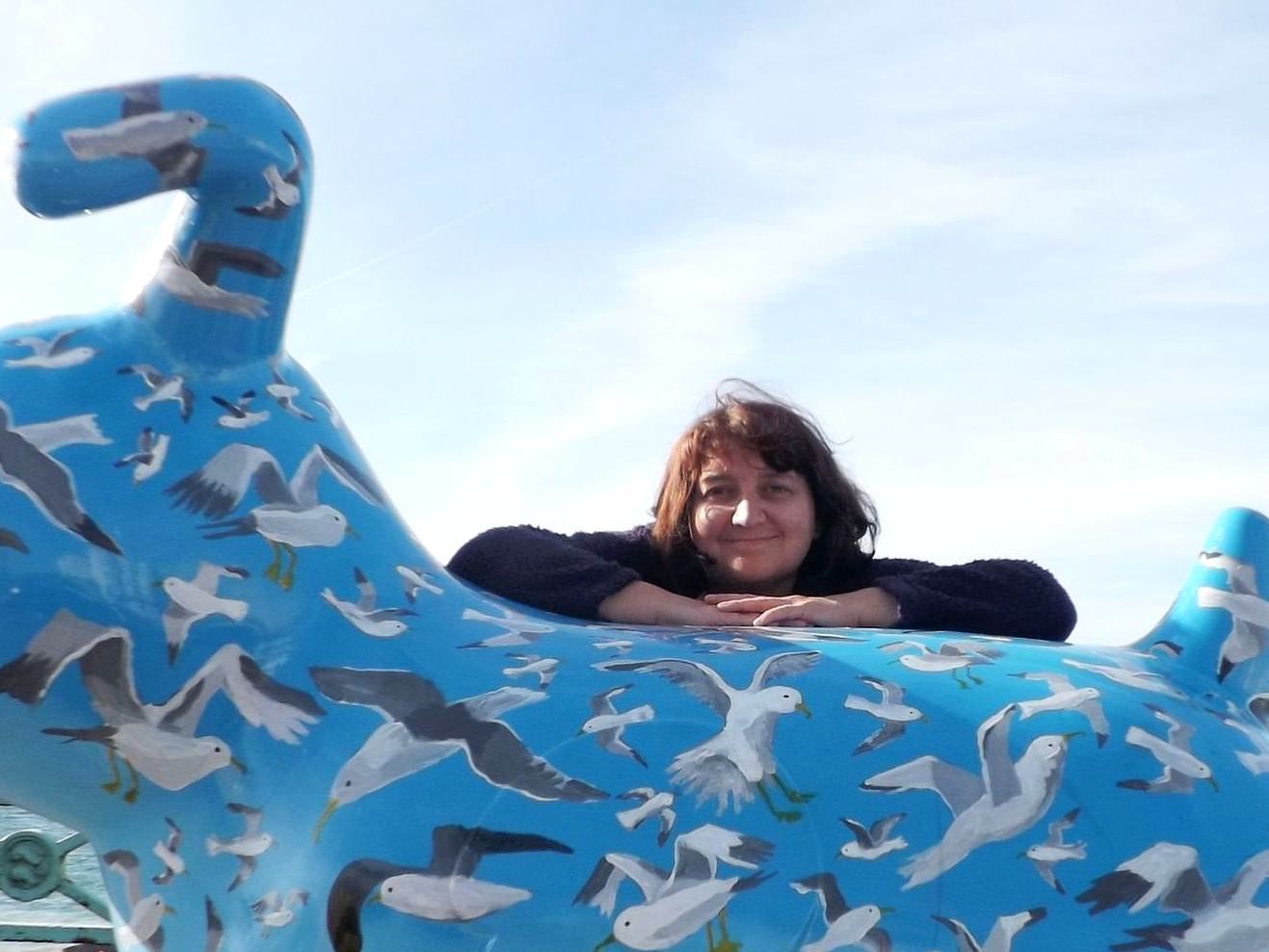 A woman leaning on a blue statue with seagulls on it