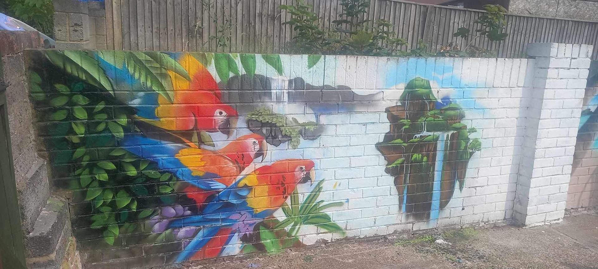 A mural of parrots and flowers on a brick wall.