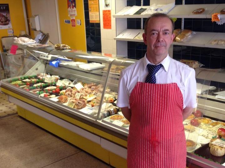 A man in an apron is standing in front of a display case of food
