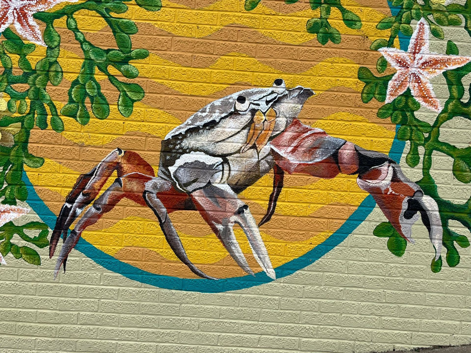 A mural of a crab and flowers on a brick wall.