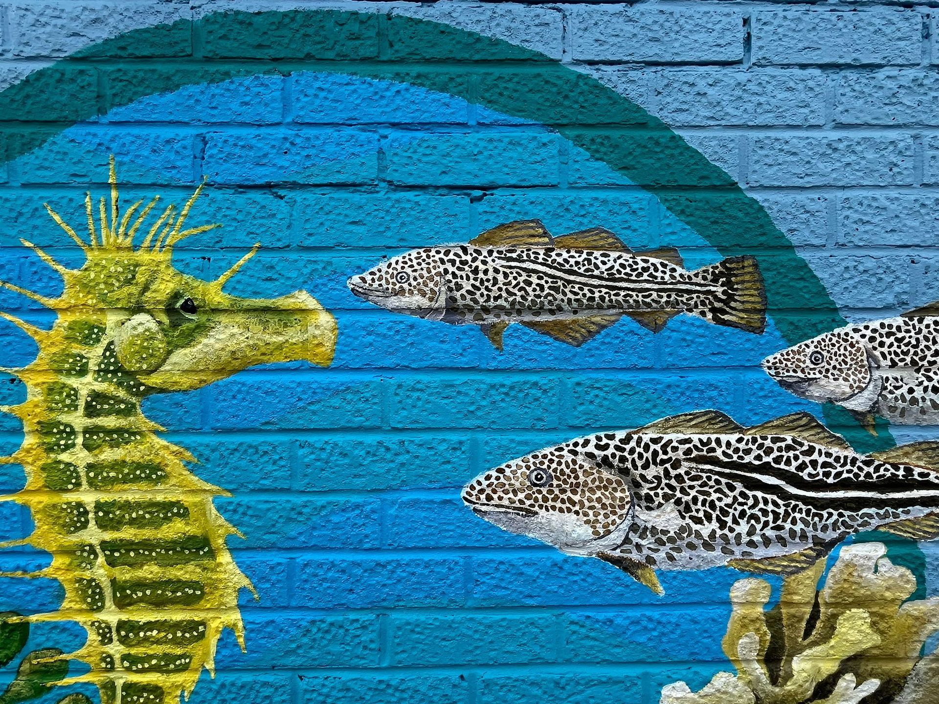 A painting of a seahorse and fish on a brick wall.
