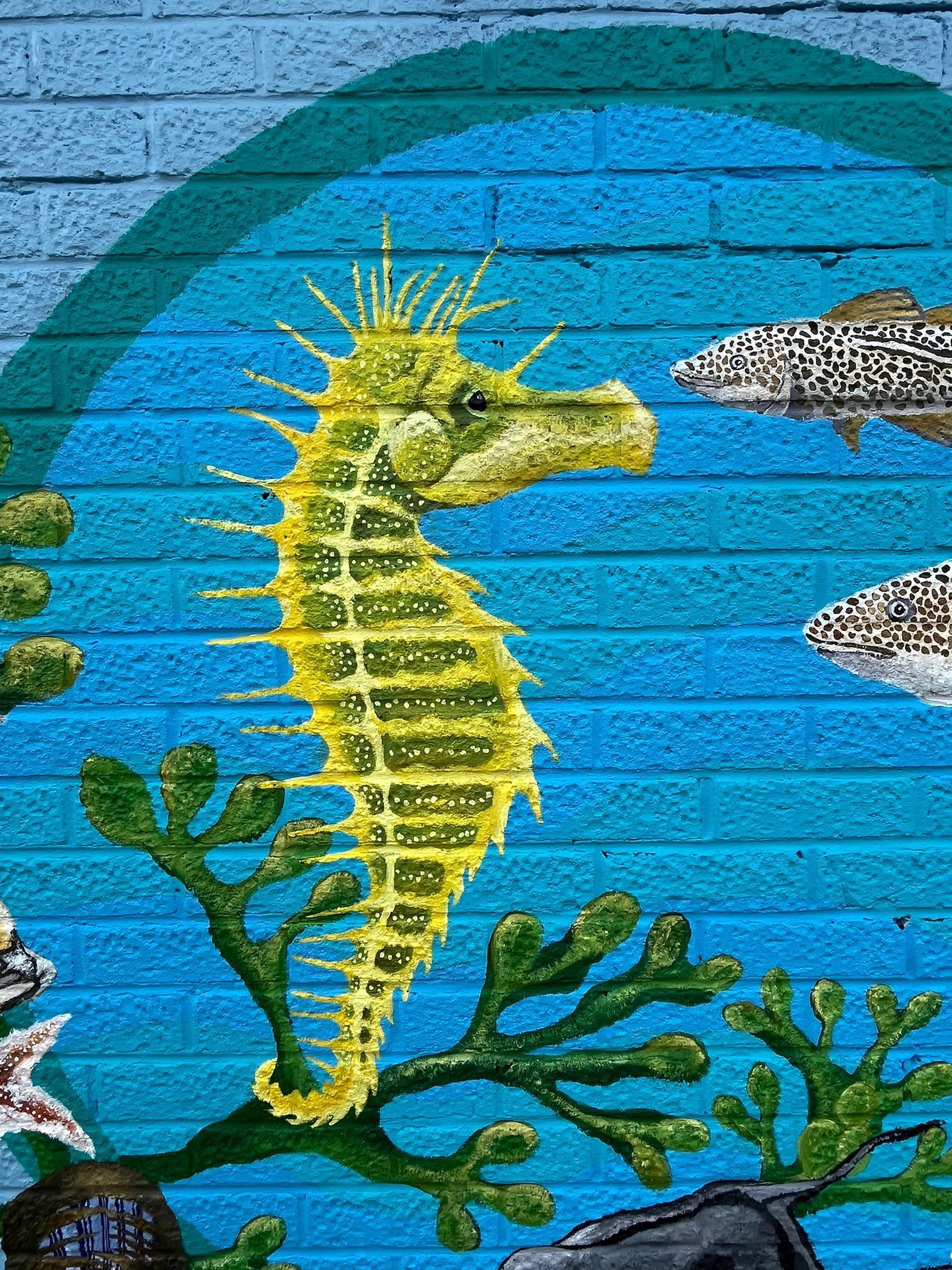 A painting of a seahorse on a blue brick wall.