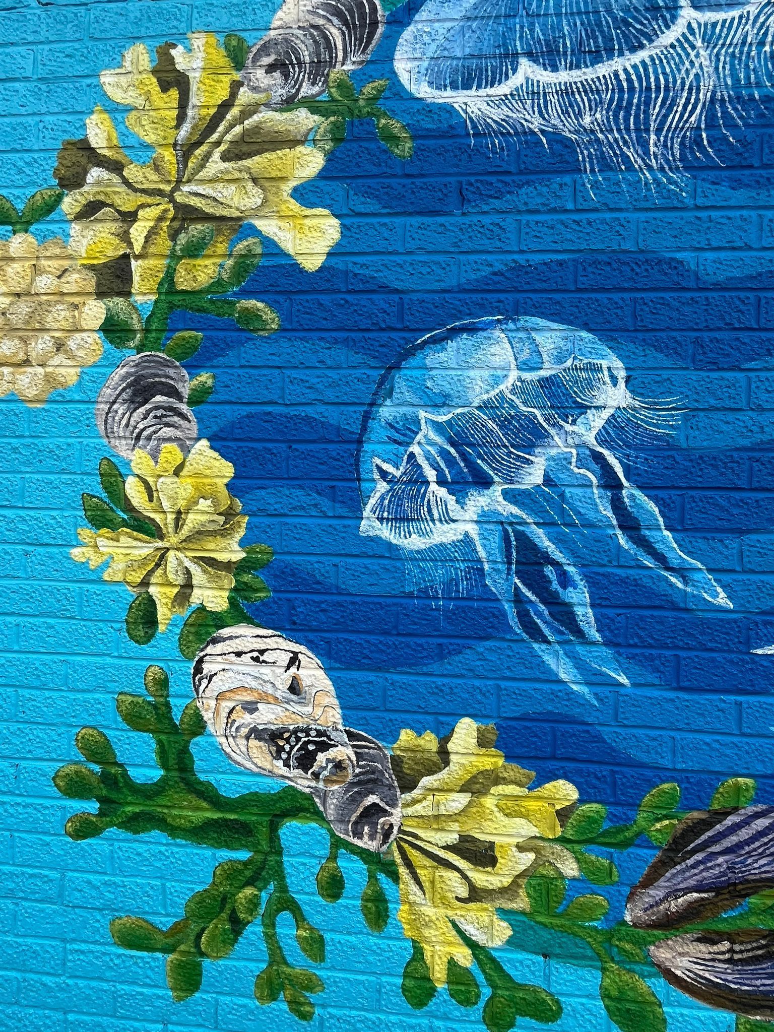 A mural of jellyfish and seaweed on a blue brick wall.