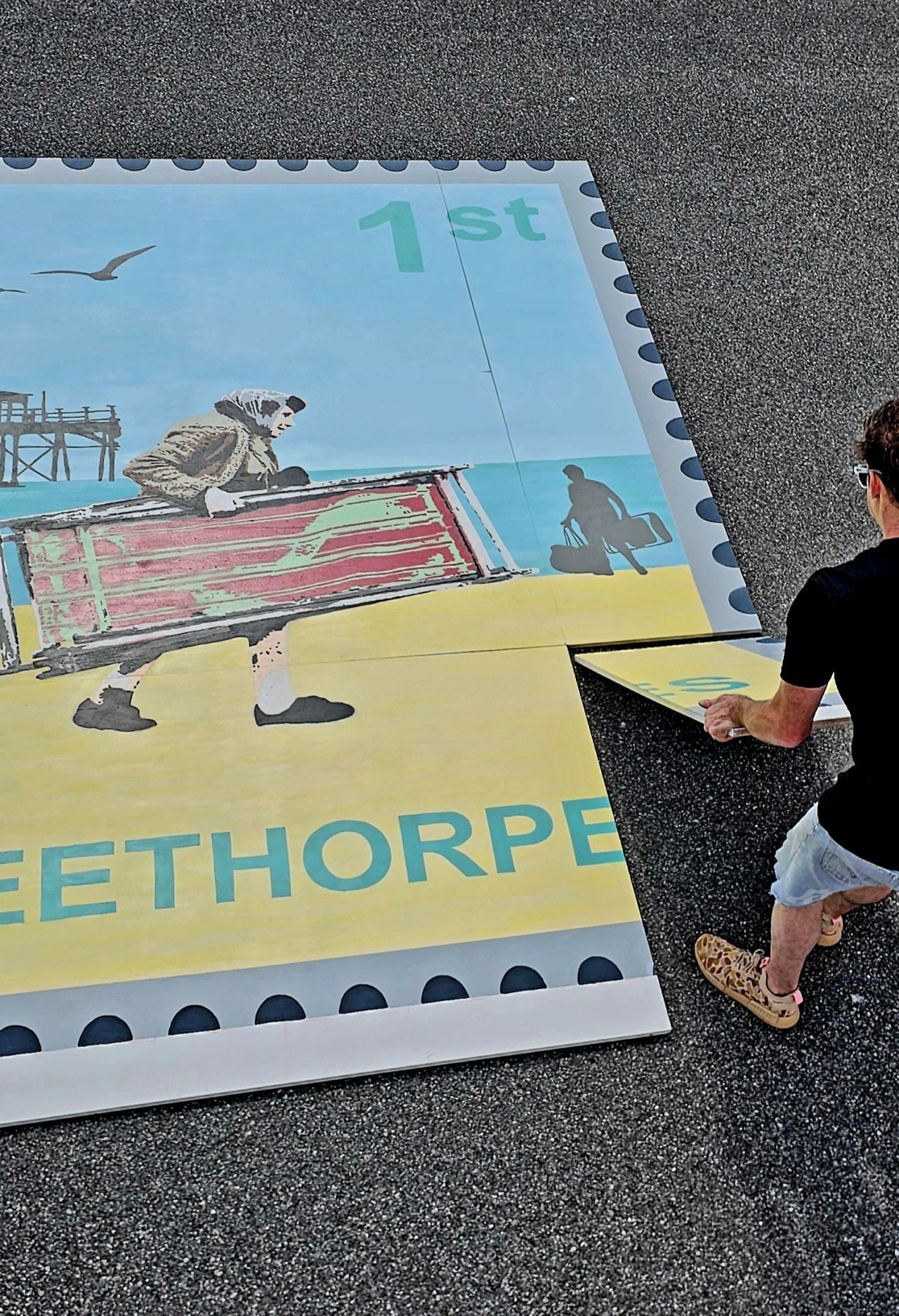 A person is standing in front of a large postage stamp that says eethorpe