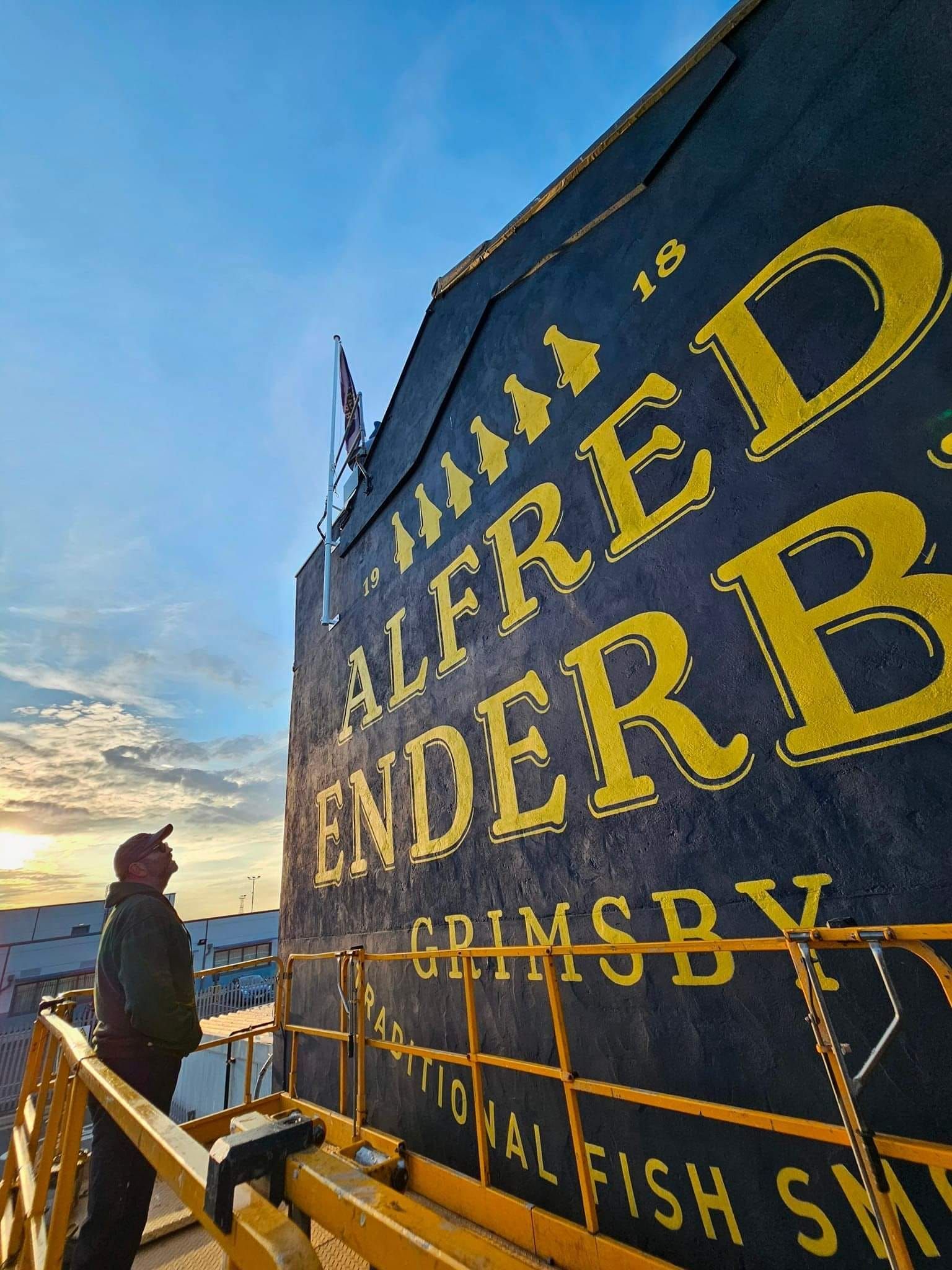 A man is standing in front of a large sign that says alfred enderby
