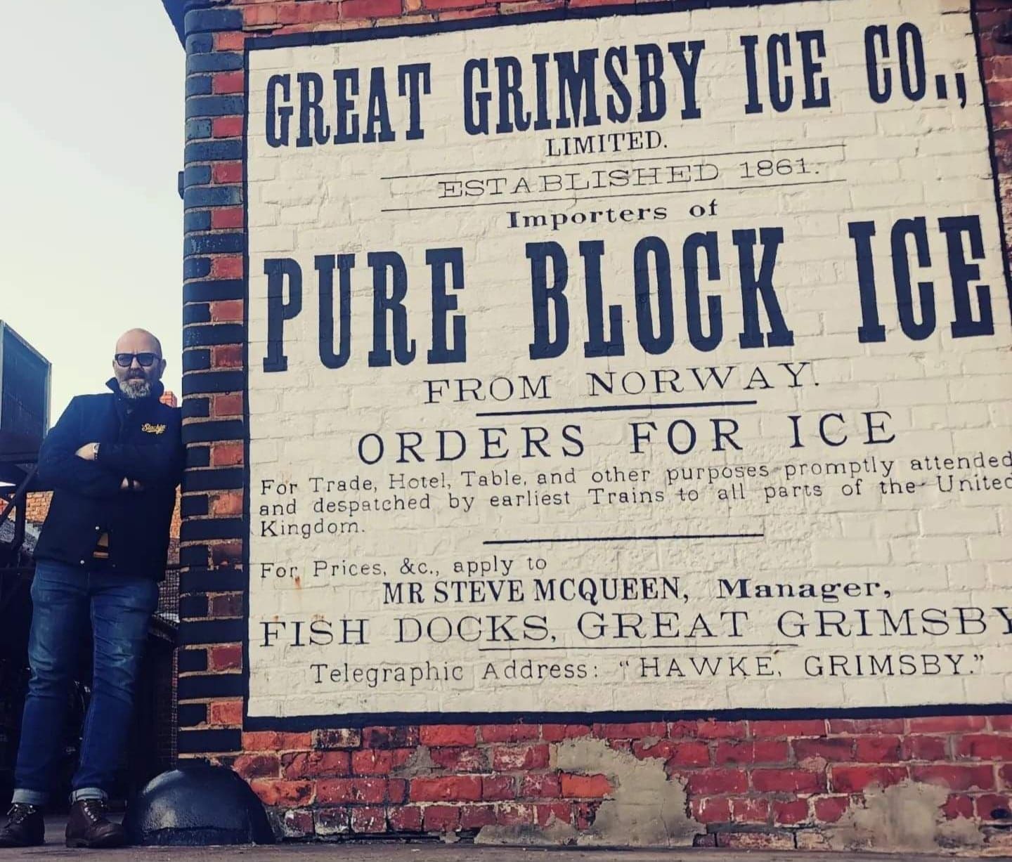 A man stands in front of a sign that says great grimsby ice co.