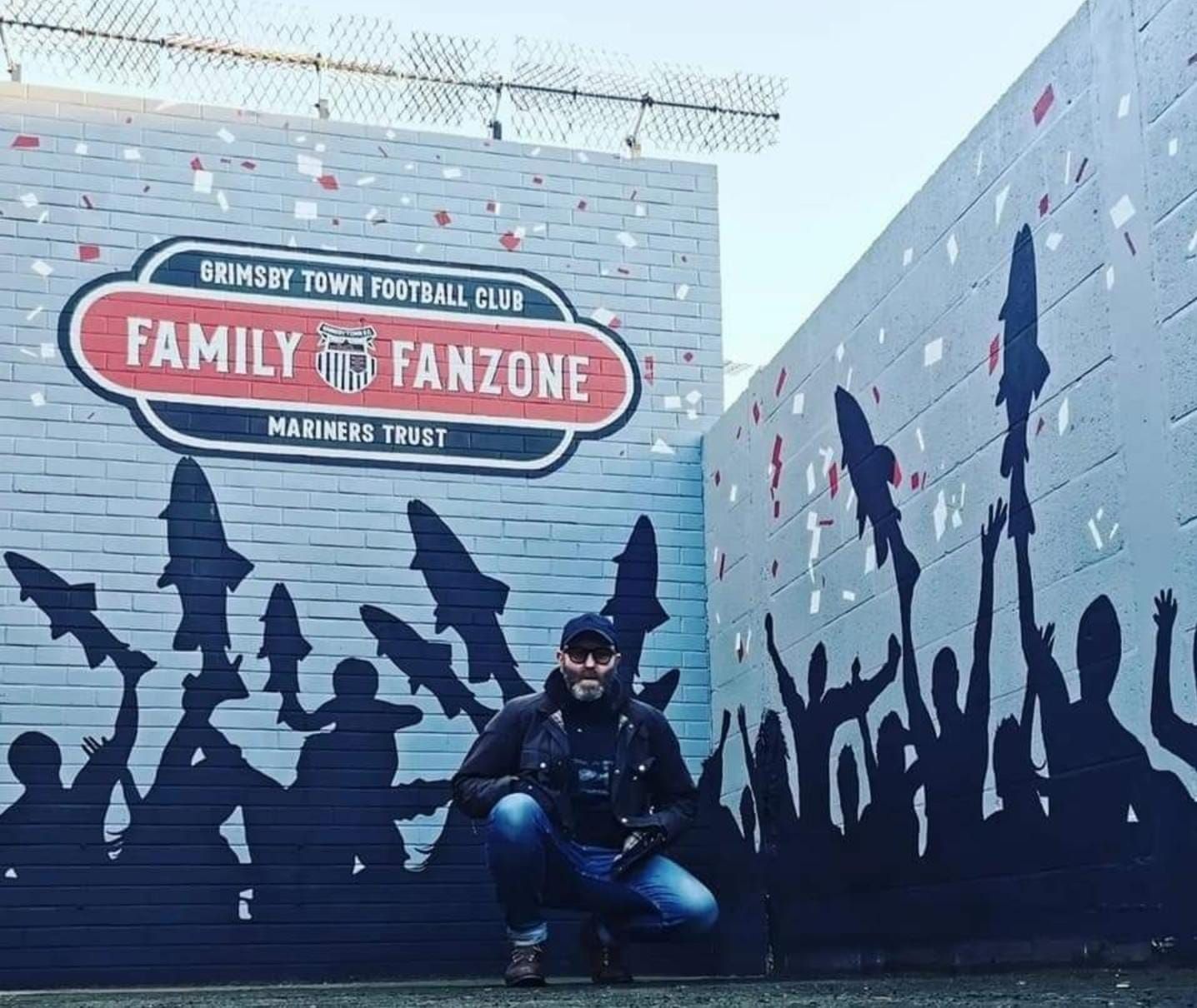 A man kneeling in front of a wall that says family fanzone