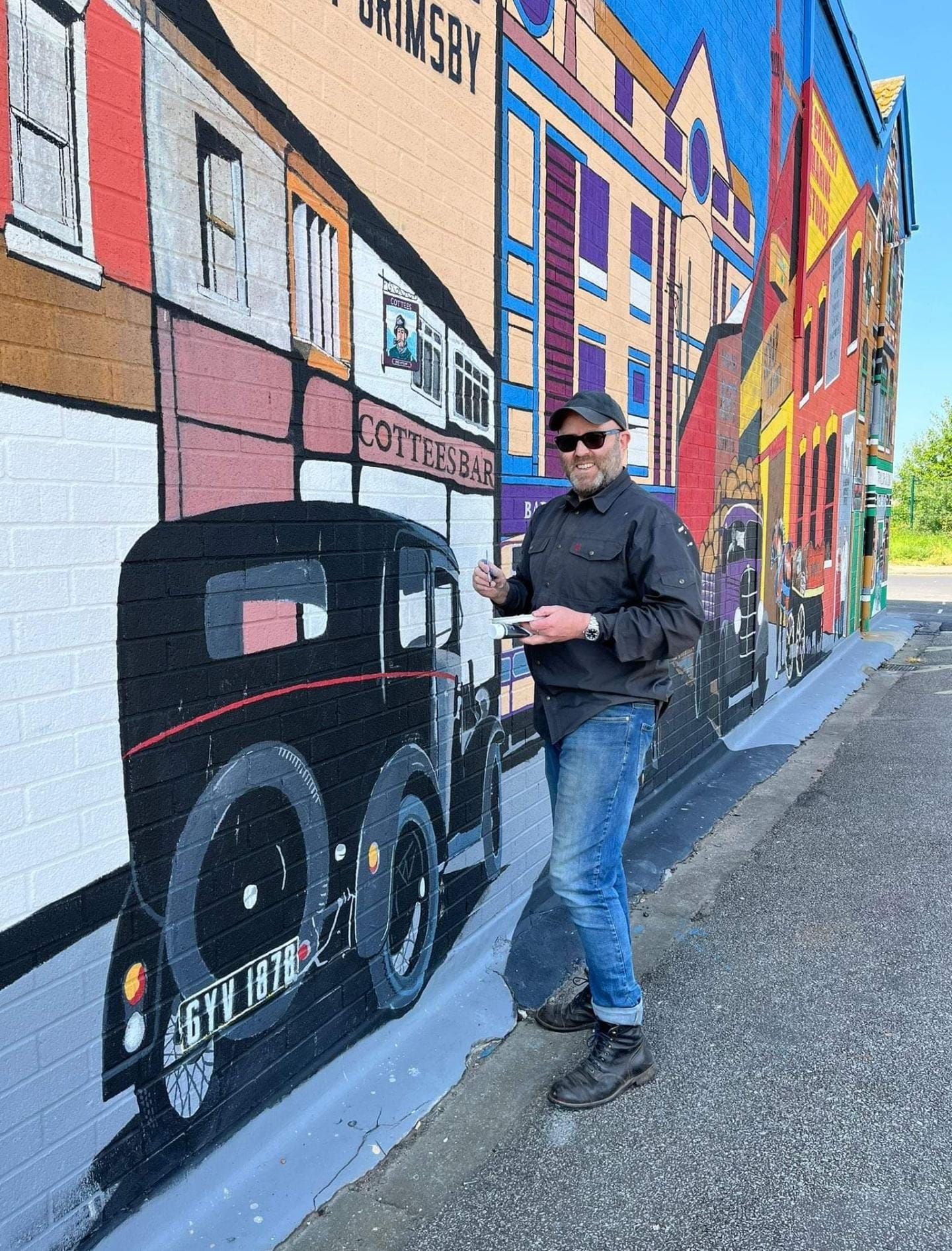 A man is standing in front of a mural on the side of a building.
