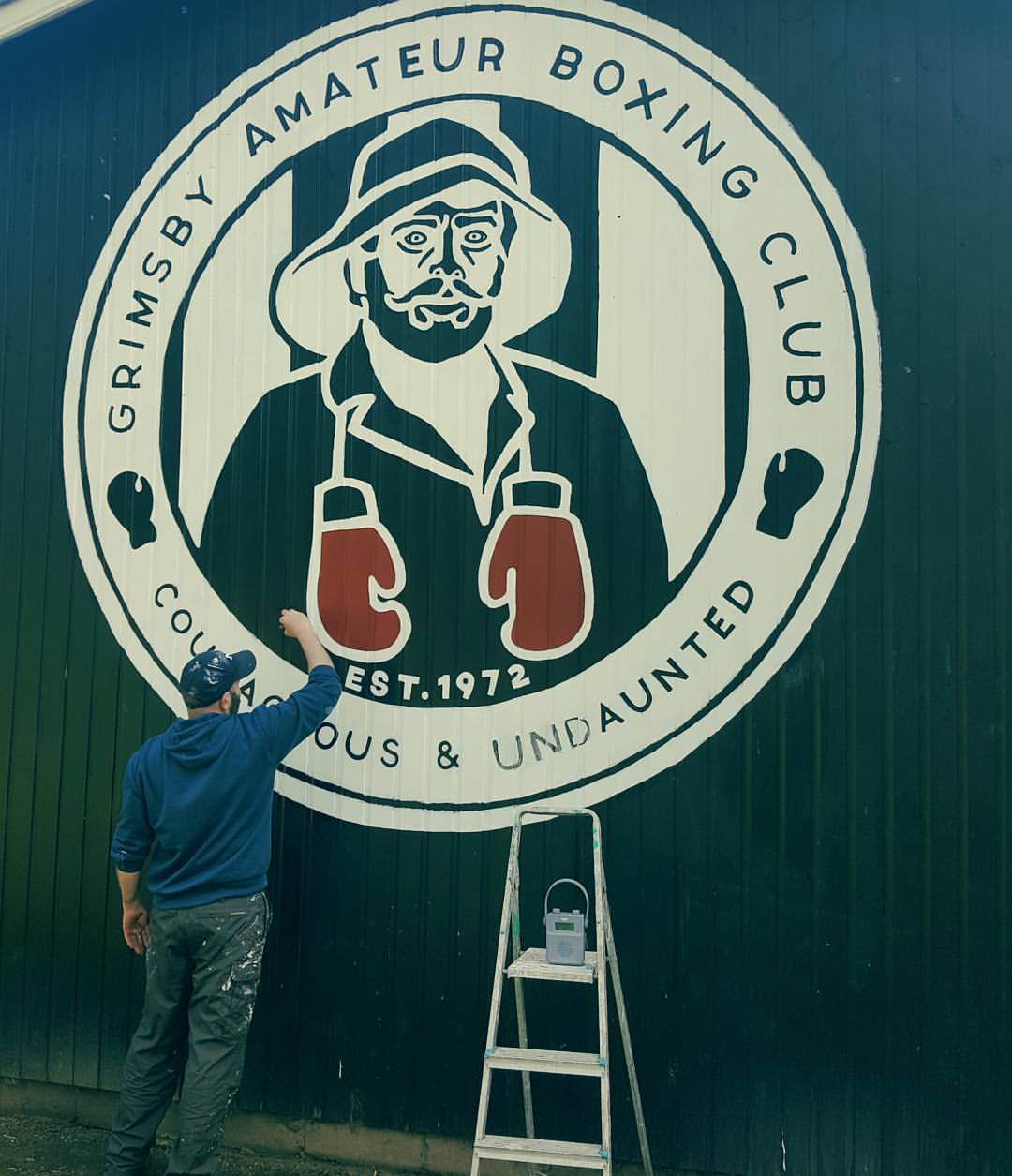 A man paints a logo for the grimsby amateur boxing club