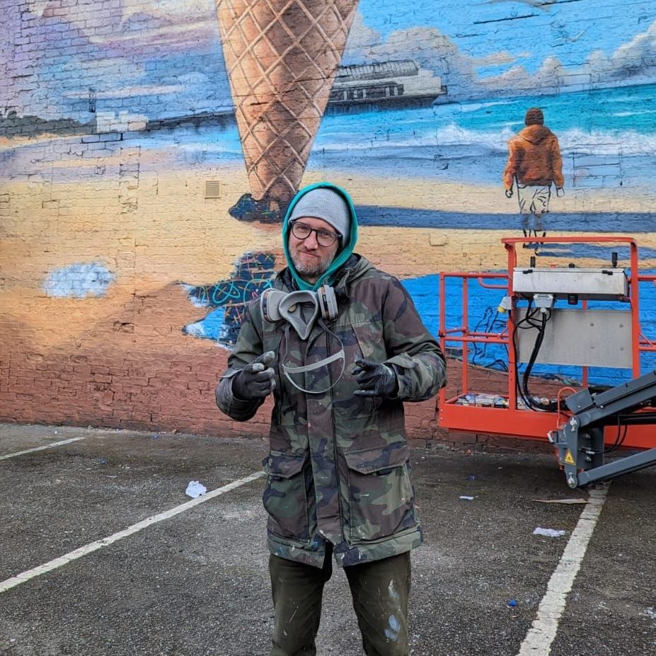 A man is standing in front of a mural of an ice cream cone on a beach.