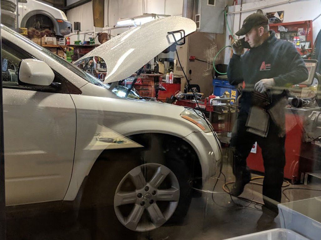 A man is working on a car in a garage with the hood up.