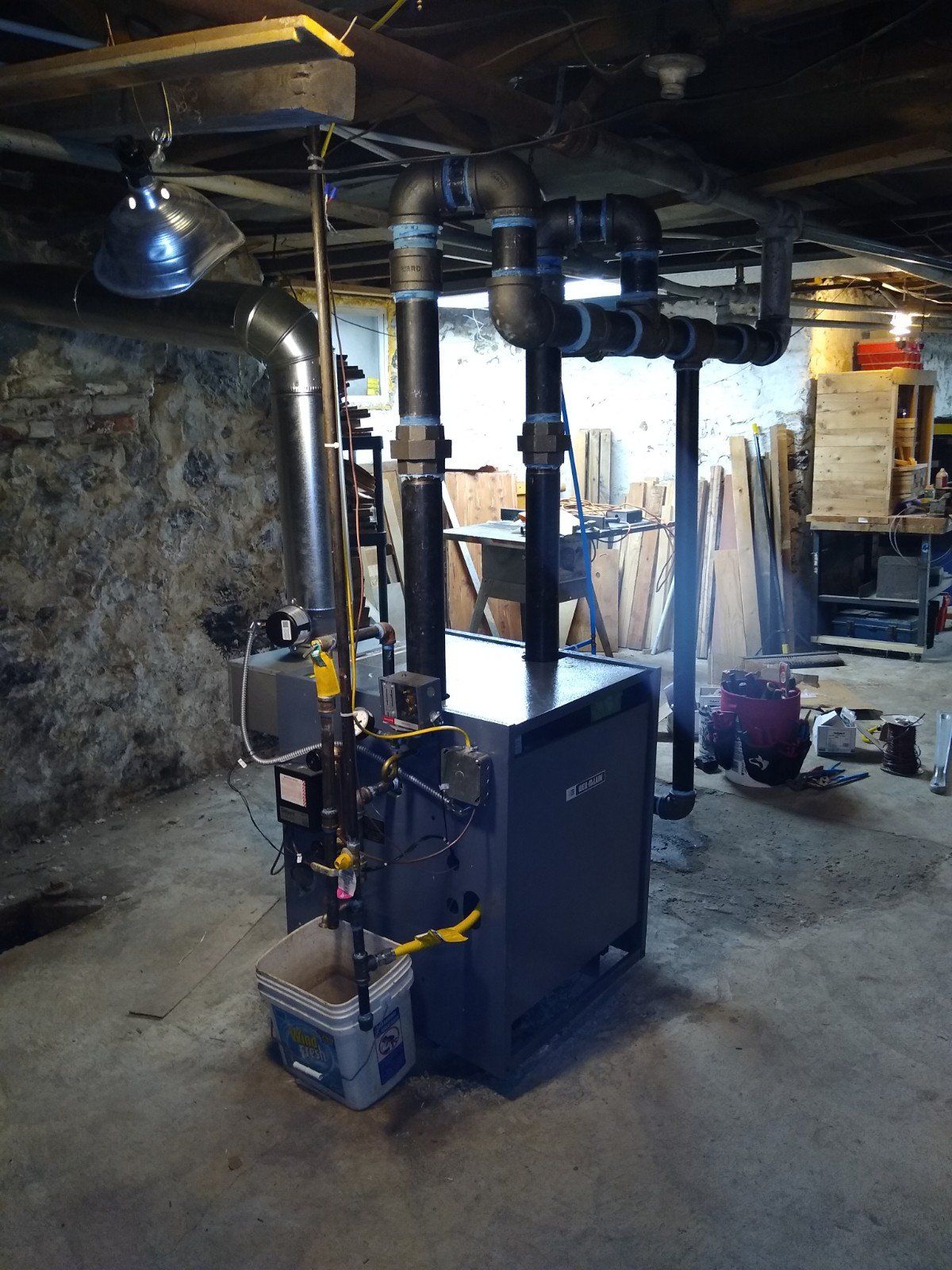 A boiler is sitting in a basement with pipes coming out of it.
