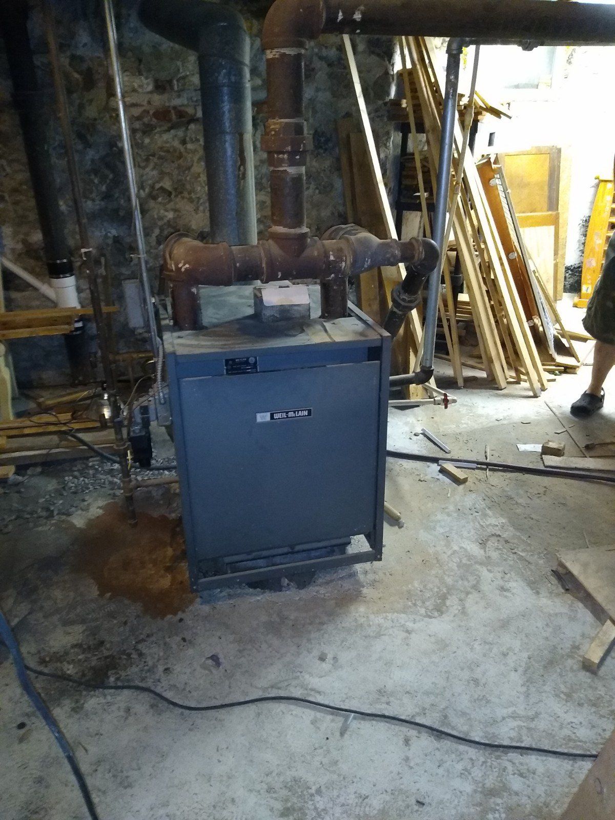 A boiler is sitting in a basement next to a pile of wood.