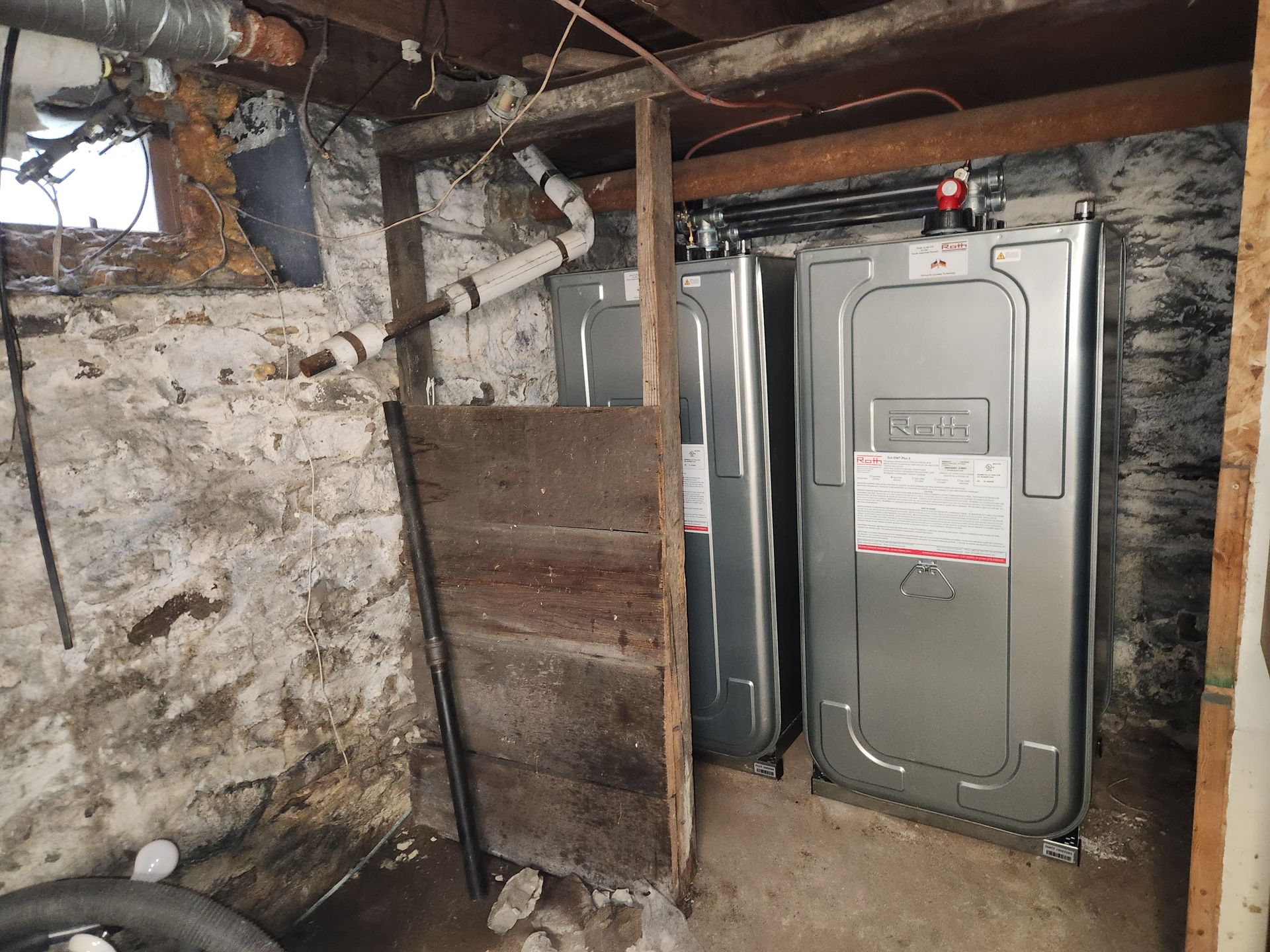 Two metal tanks are sitting in a basement next to a wooden wall.