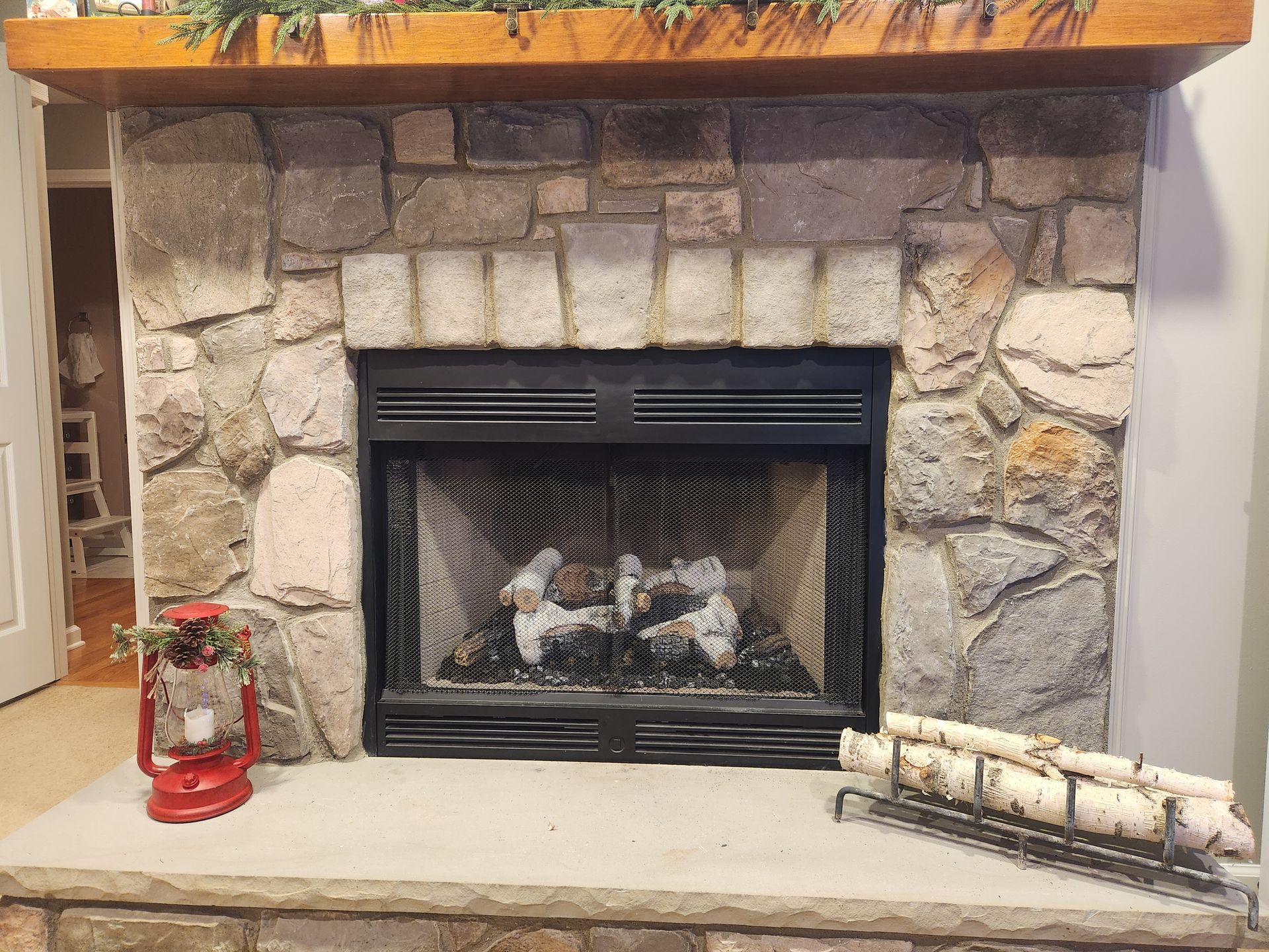 A stone fireplace with a wooden mantle and a lantern on the mantle.