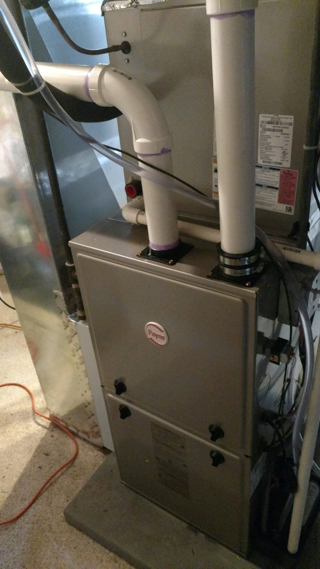 A stainless steel furnace is sitting in a basement next to a refrigerator.