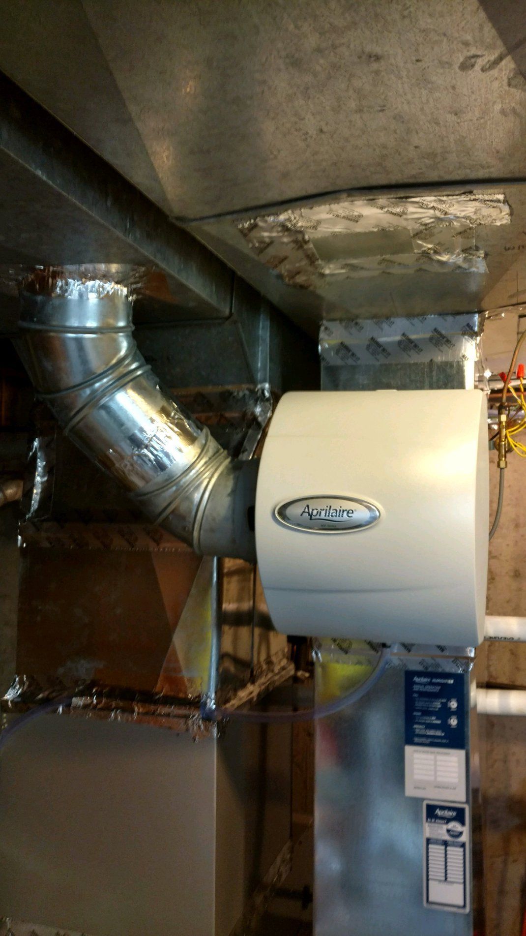 A white air conditioner is sitting in a basement next to a pipe.