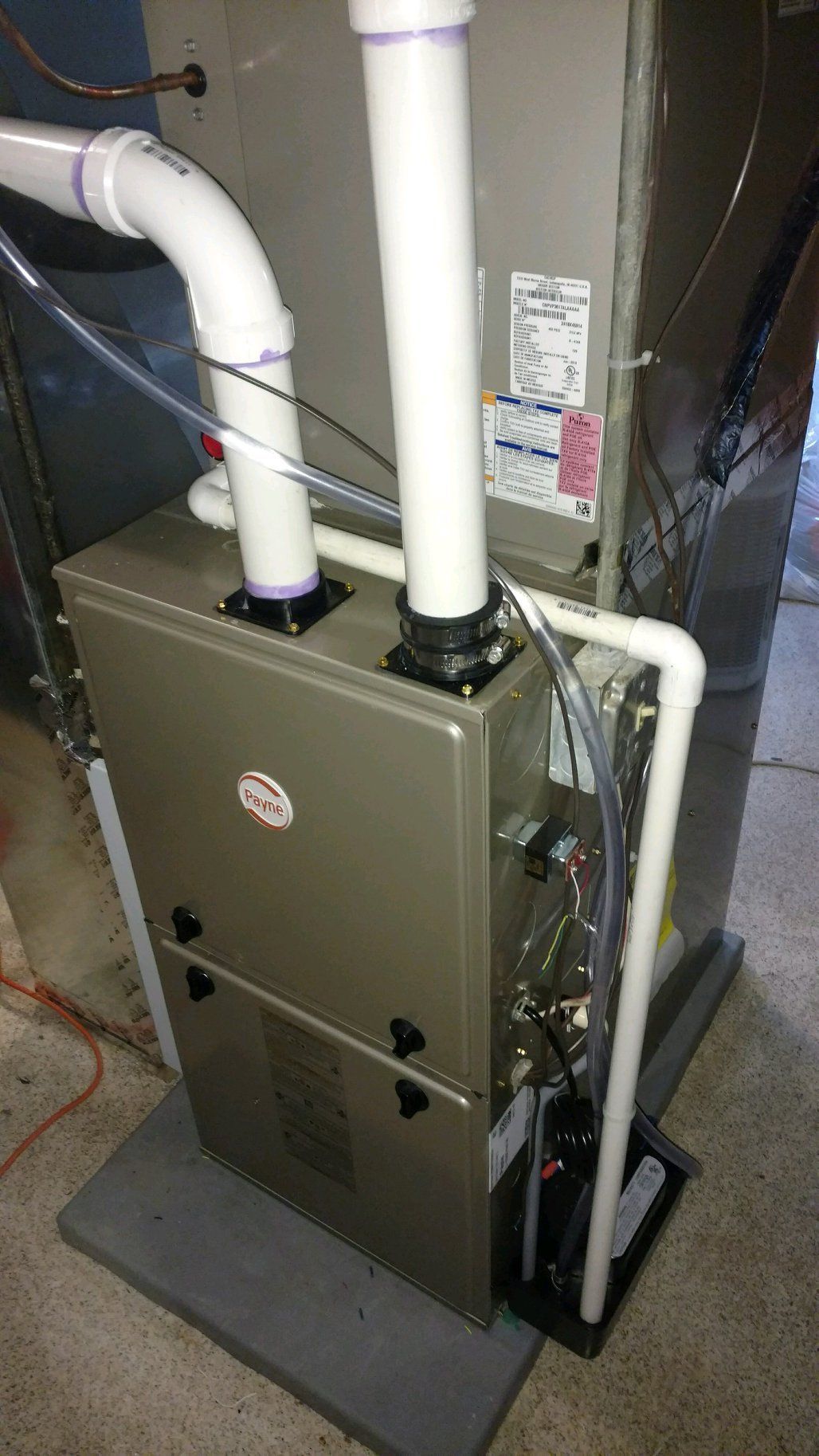 A furnace is sitting in a basement next to a pipe.