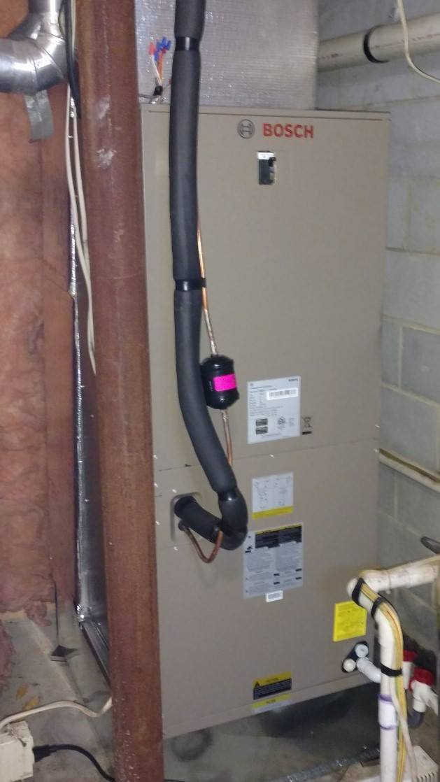 A bosch air conditioner is sitting in a basement next to a pipe.