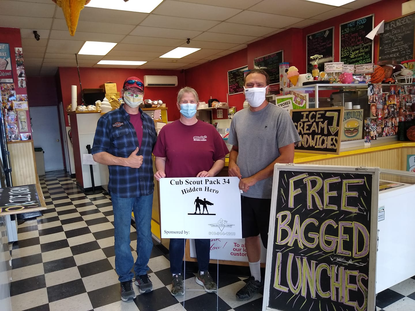 Three people wearing face masks are standing in a restaurant holding a sign that says free bagged lunches.