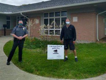 Two men wearing masks are standing in front of a building holding a sign.
