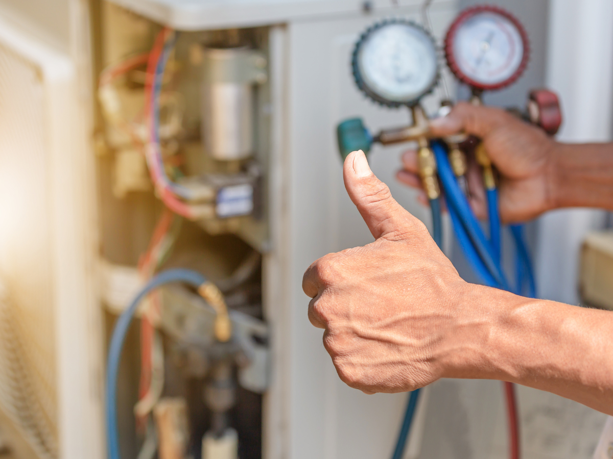 A man is giving a thumbs up while working on an air conditioner.