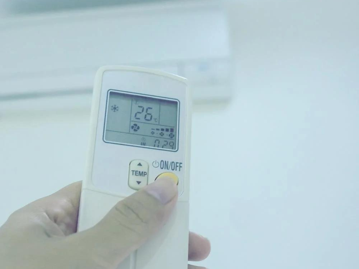 A person is holding a remote control in front of an air conditioner.