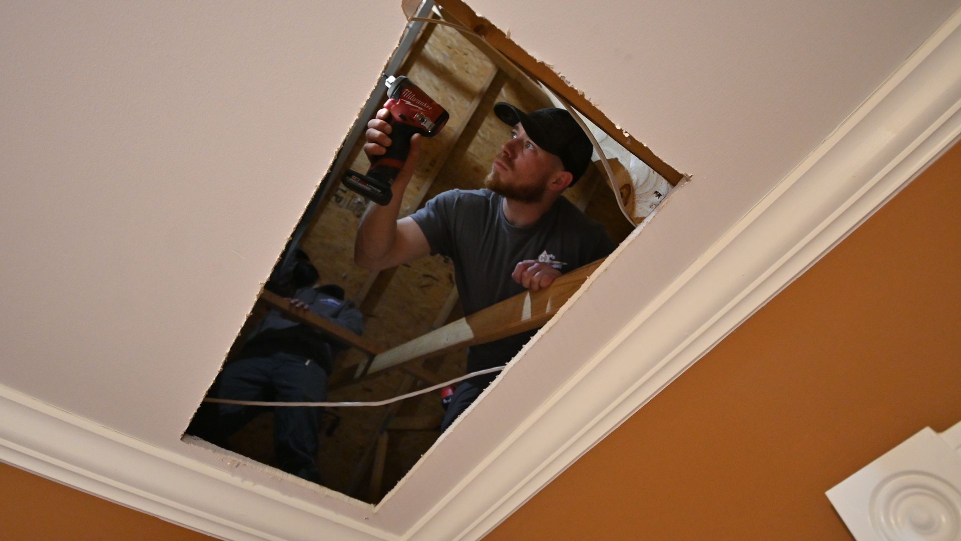 A man is using a drill to fix a hole in the ceiling.