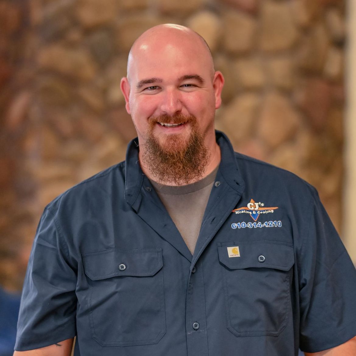 A bald man with a beard wearing a blue shirt that says ' carhartt ' on it