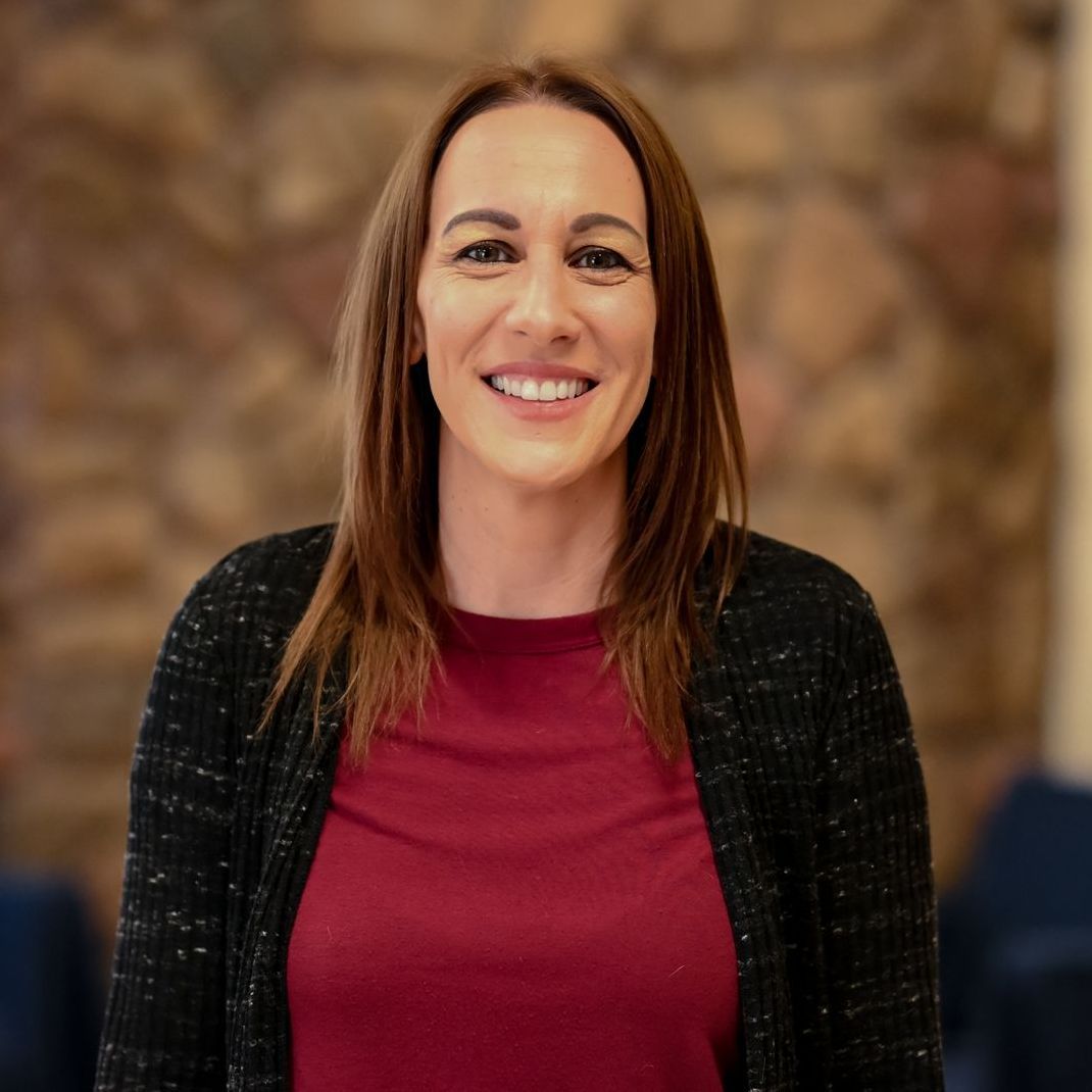 A woman in a red shirt and black cardigan is smiling for the camera.