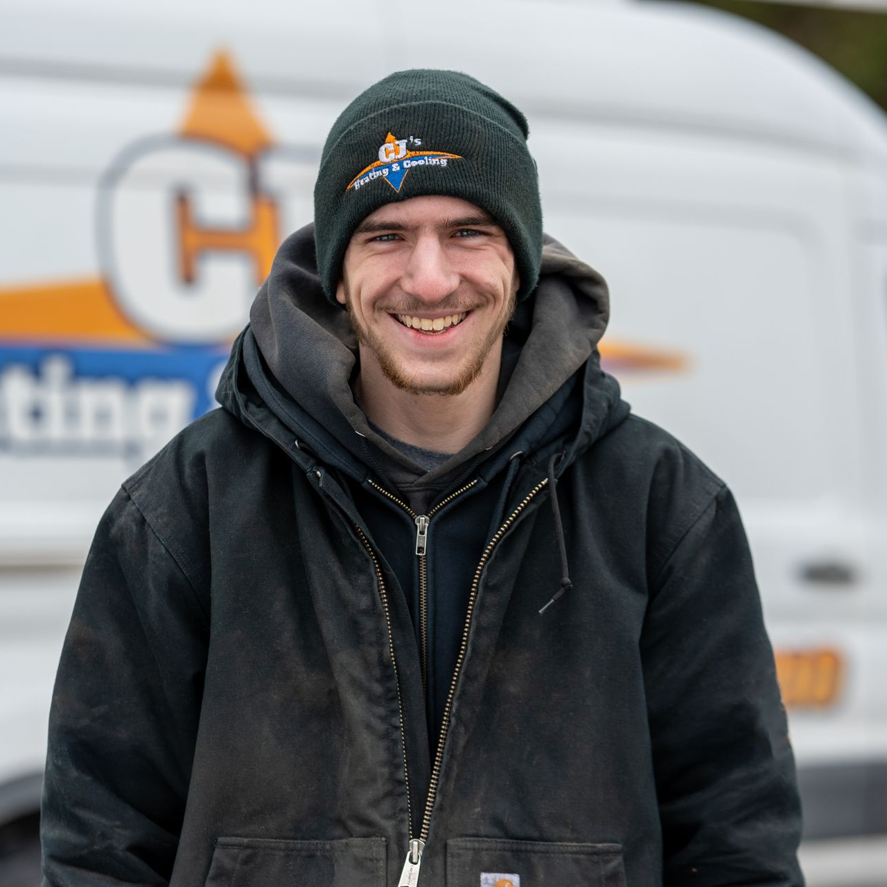 Man in black beanie and jacket smiling in front of a white van with orange and blue logo.