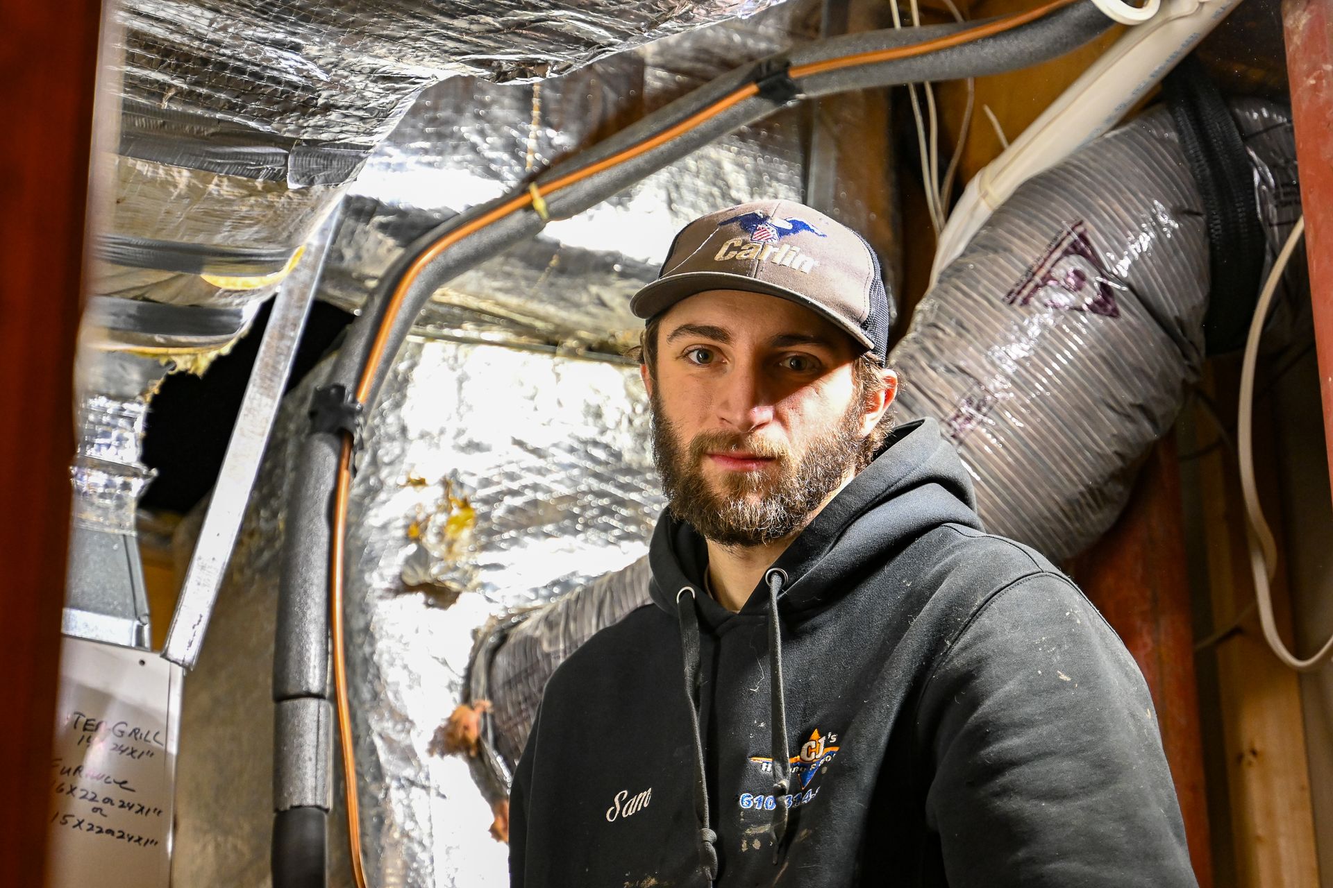 A man with a beard wearing a hat and a hoodie is standing in a room.