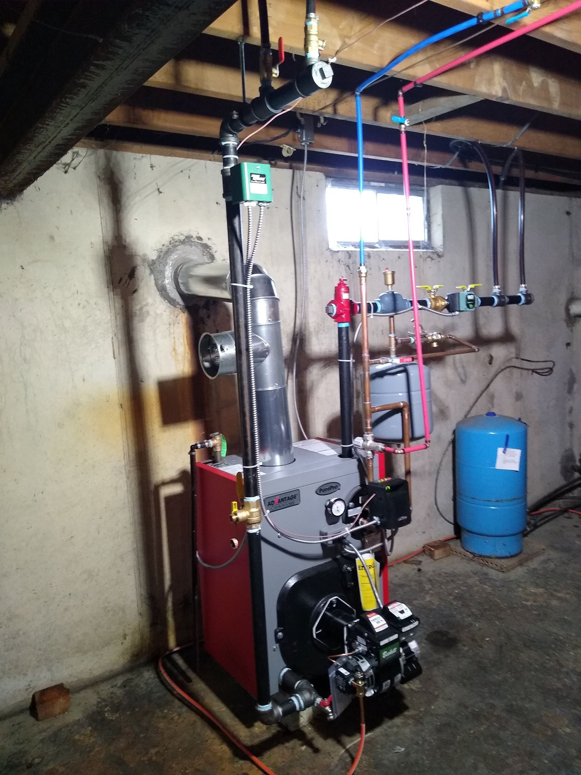 A boiler is sitting in a basement next to a blue tank