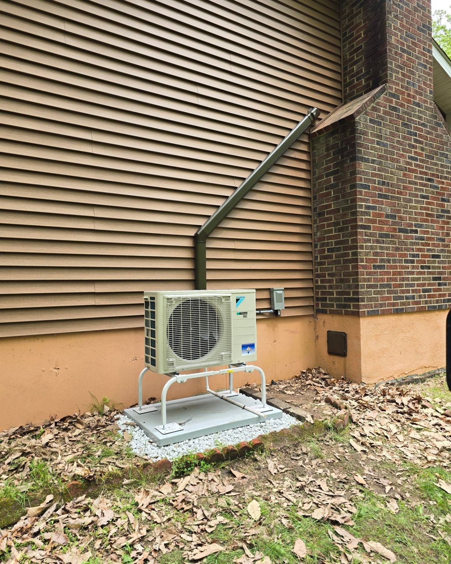 An air conditioner is sitting outside of a house next to a brick chimney.