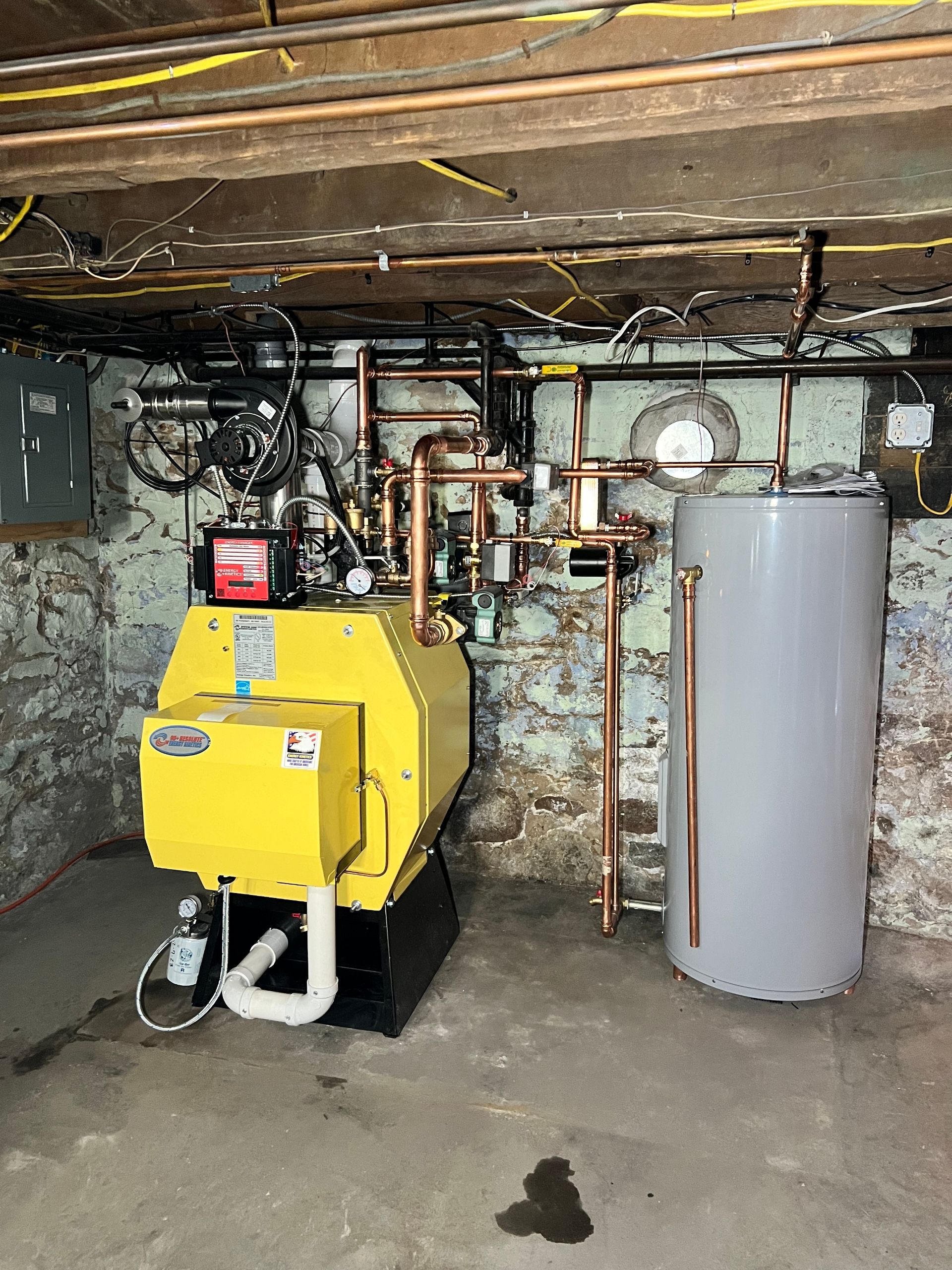 A yellow boiler and a gray water heater are in a basement.