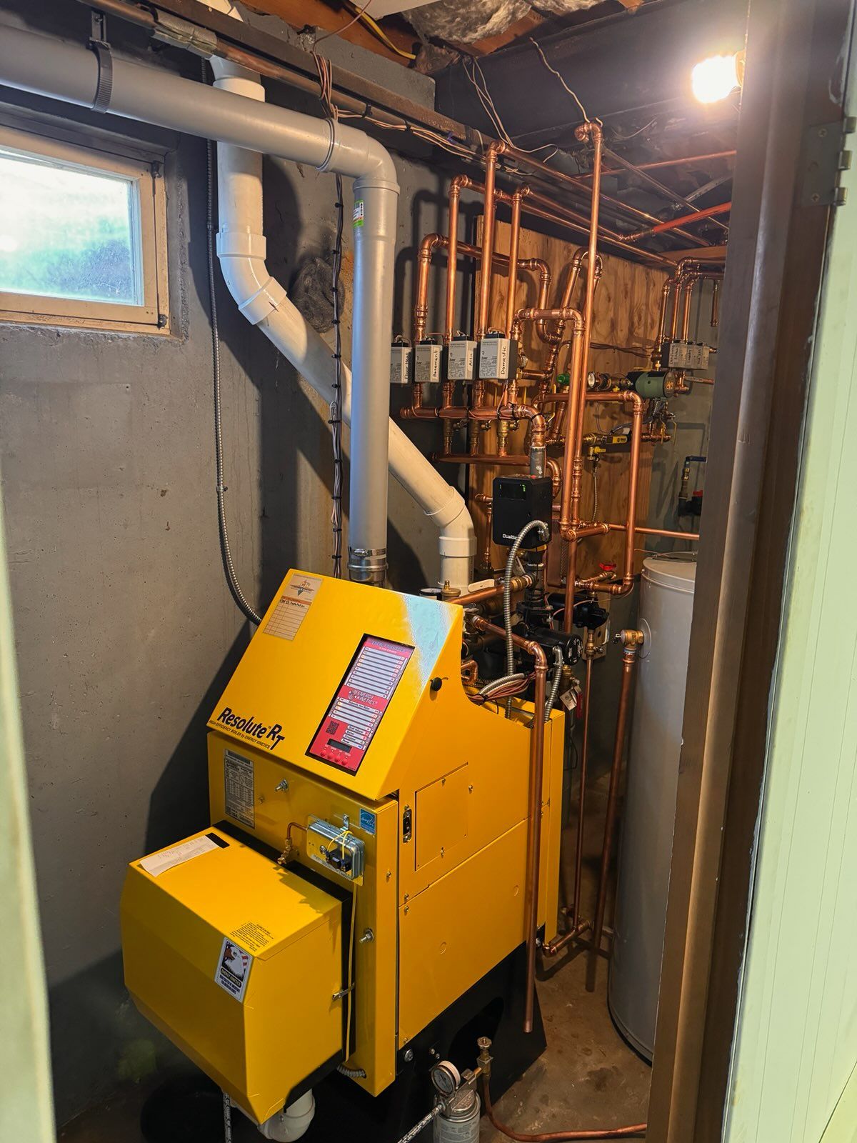 A yellow boiler is sitting in a basement next to a window.