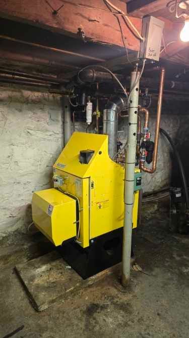A yellow boiler is sitting in a basement next to a pole.