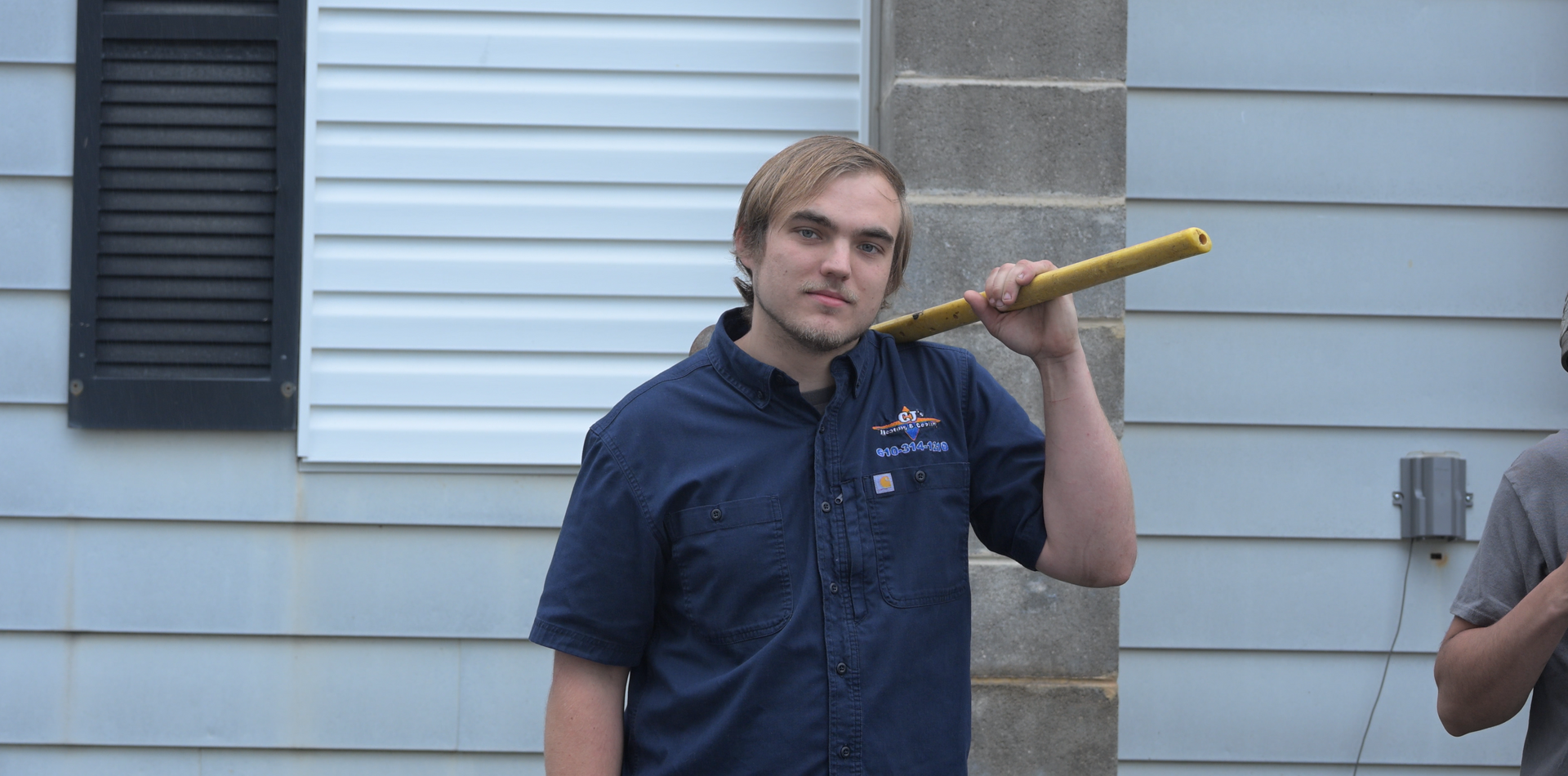 A man in a blue shirt is holding a yellow stick in front of a house.