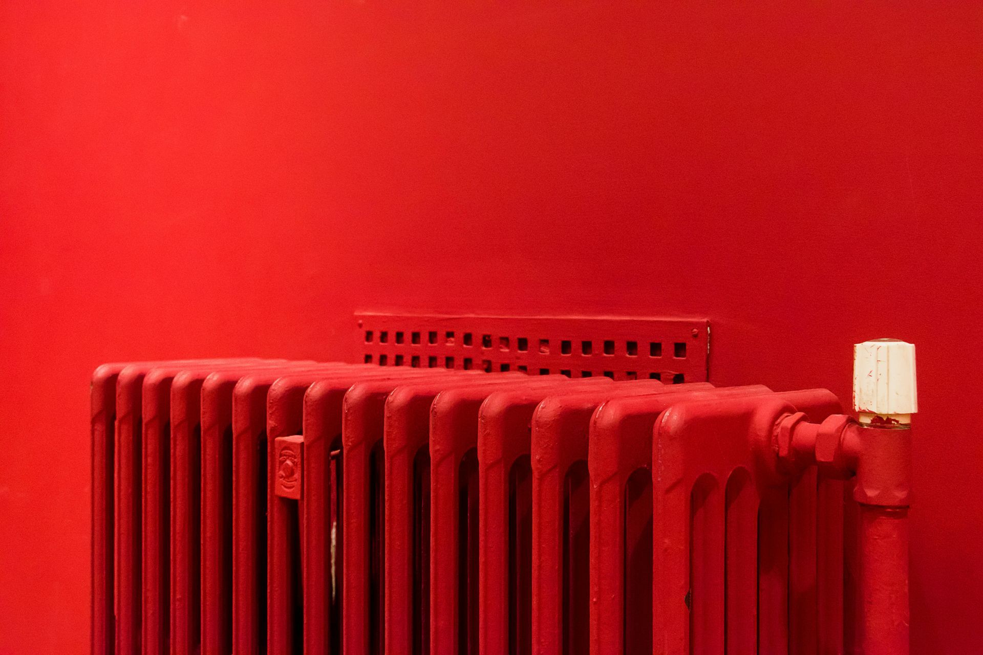 A red radiator is sitting in front of a red wall.