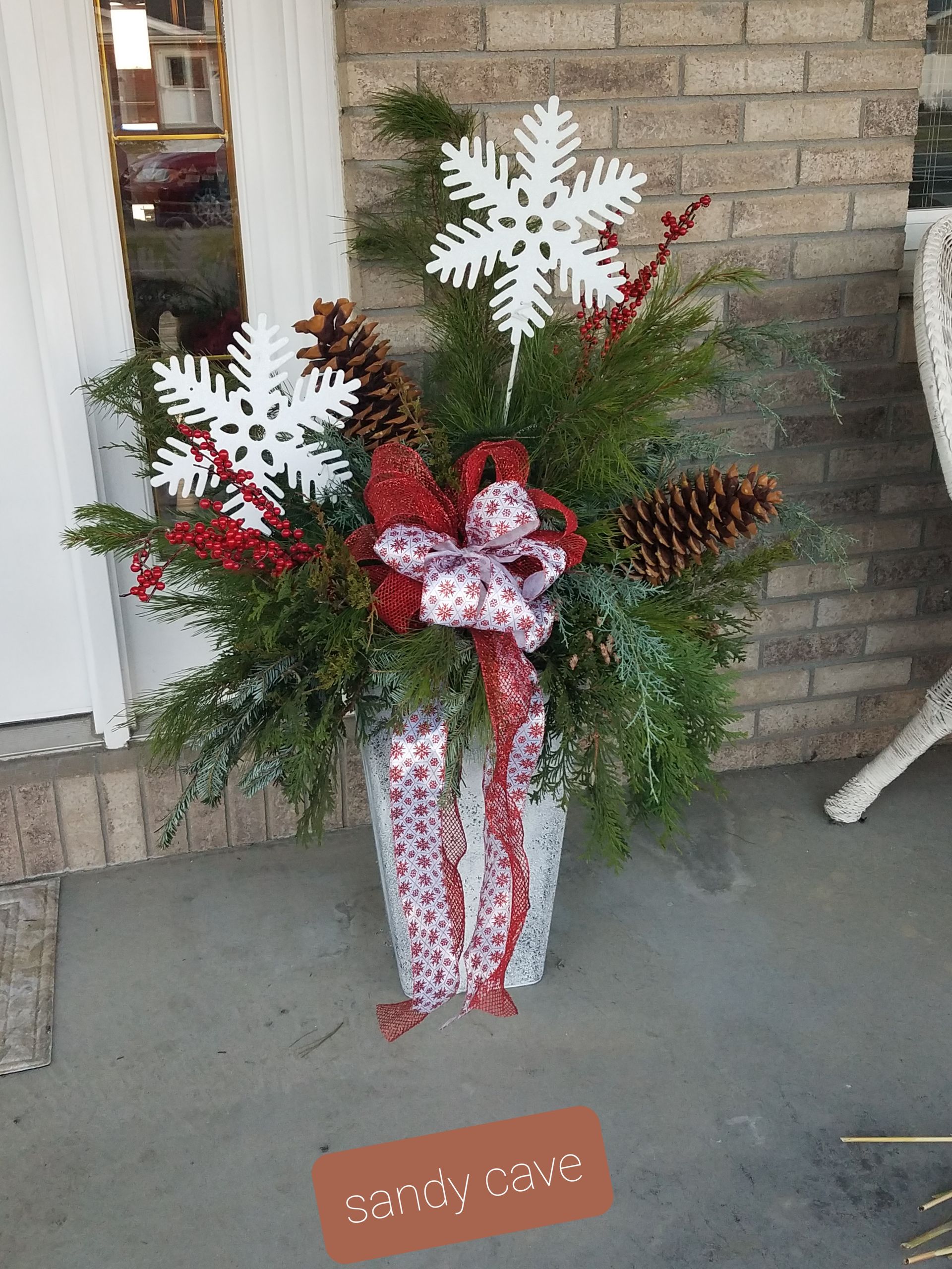 A large vase filled with christmas decorations is sitting on a porch.