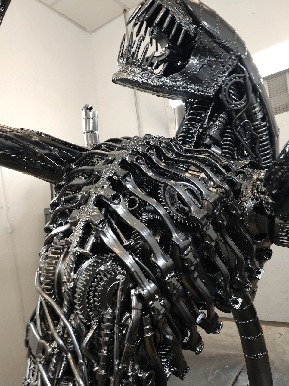 A statue of an alien made out of metal is sitting in a room.