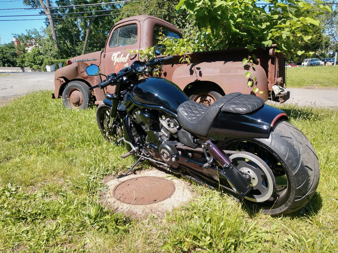 A motorcycle is parked in the grass next to an old rusty truck.