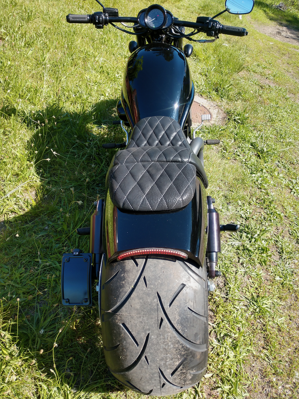 The back of a black motorcycle is parked in the grass.