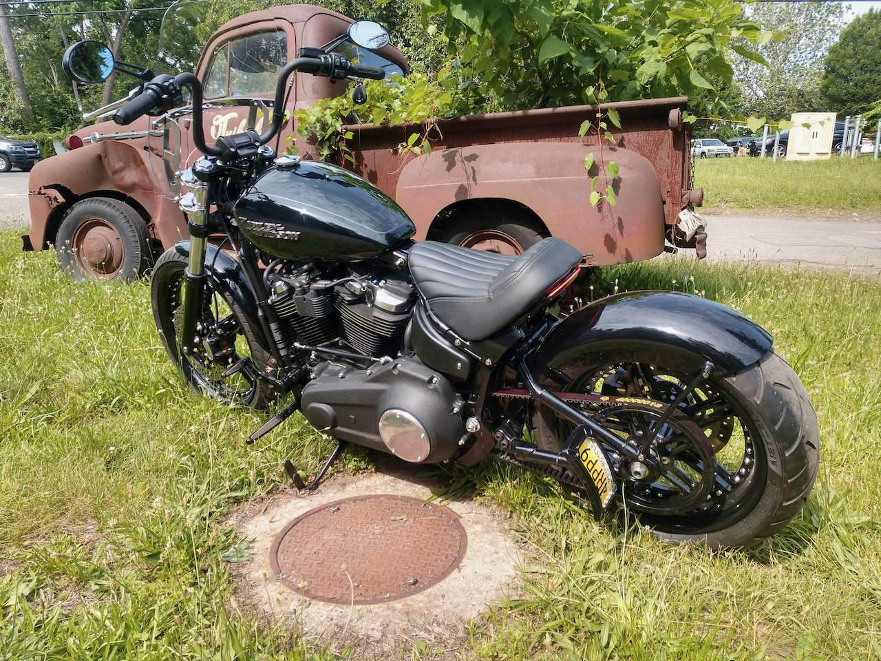 A black motorcycle is parked in the grass next to an old rusty truck.