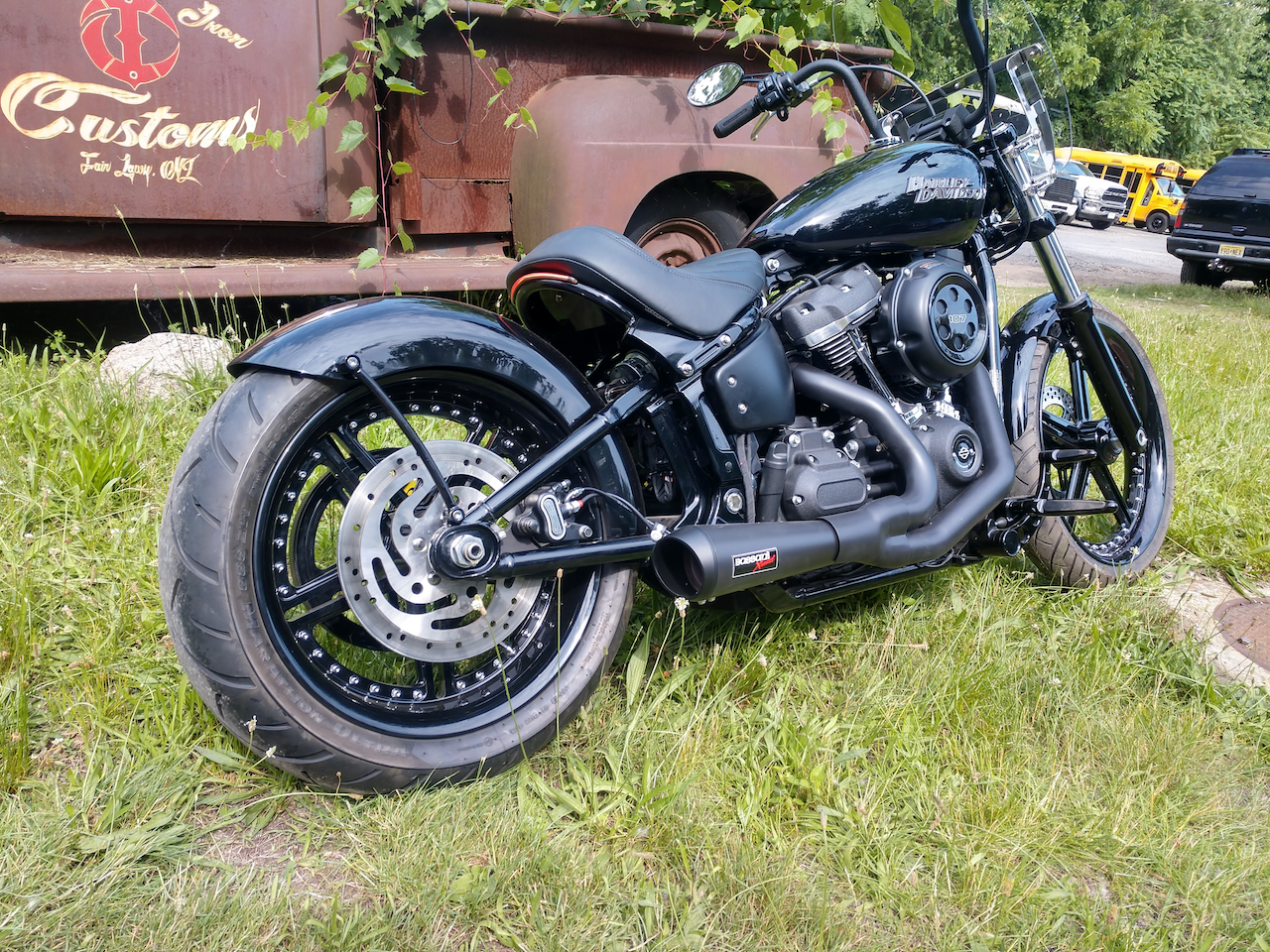A black motorcycle is parked in the grass in front of a rusty truck.