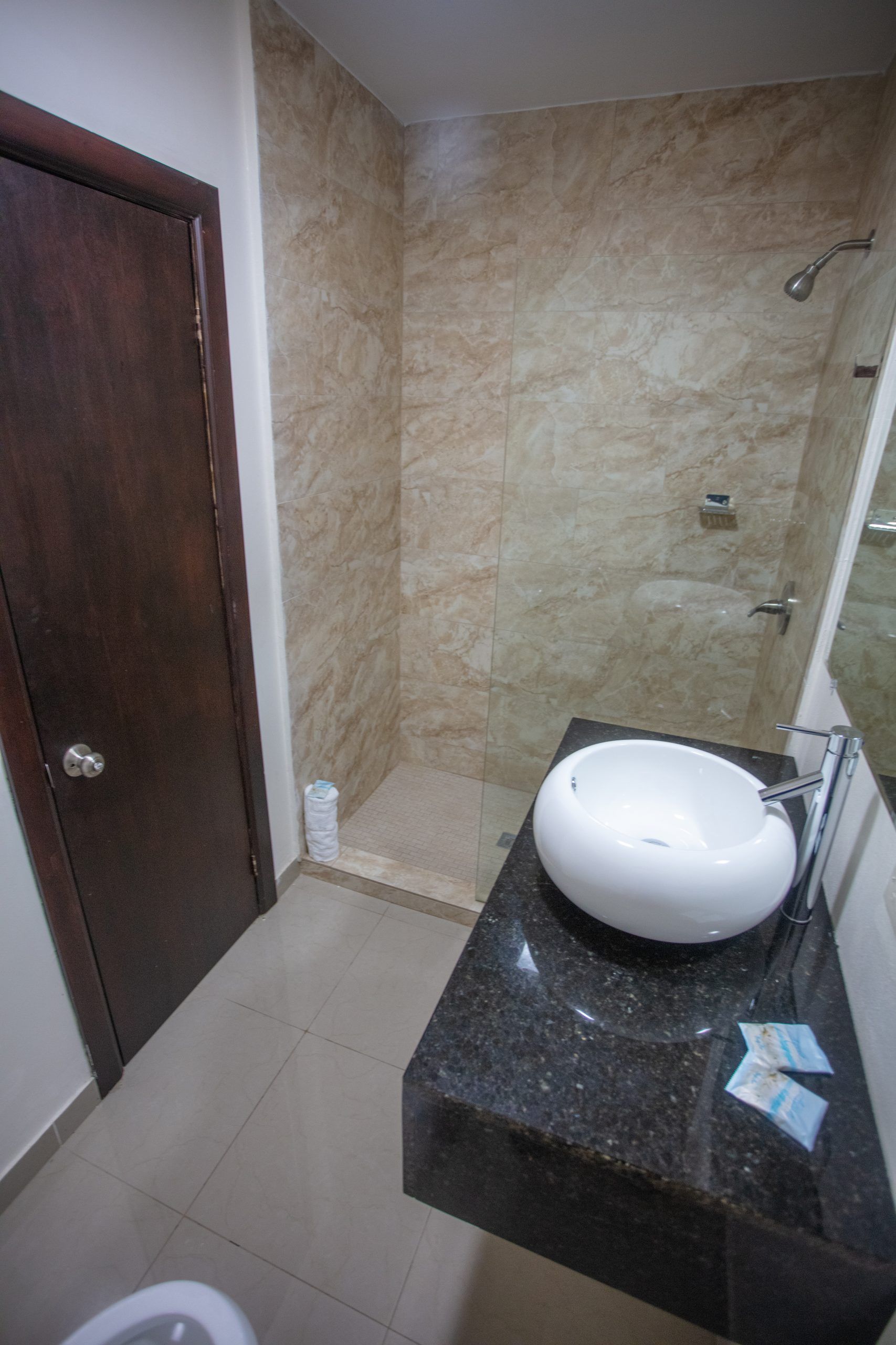 Dining area with tables, chairs, and a built-in booth. Light-colored walls and flooring. An exit door is visible.