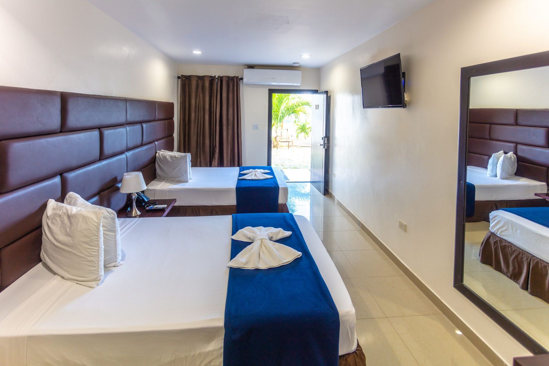 Swimming pool in front of a tan hotel building with palm trees.