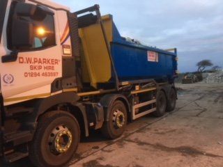 White truck with blue skip on trailer